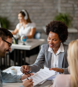 Black happy financial advisor closing a deal with a couple and pointing at the place they need to sign.