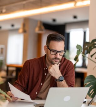 Front,View,Of,Serious,Millennial,Man,Using,Laptop,Sitting,At