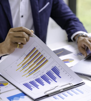 Business woman shows at graph on laptop and writing into notes or notebook.Computer screen with graphics and chart.